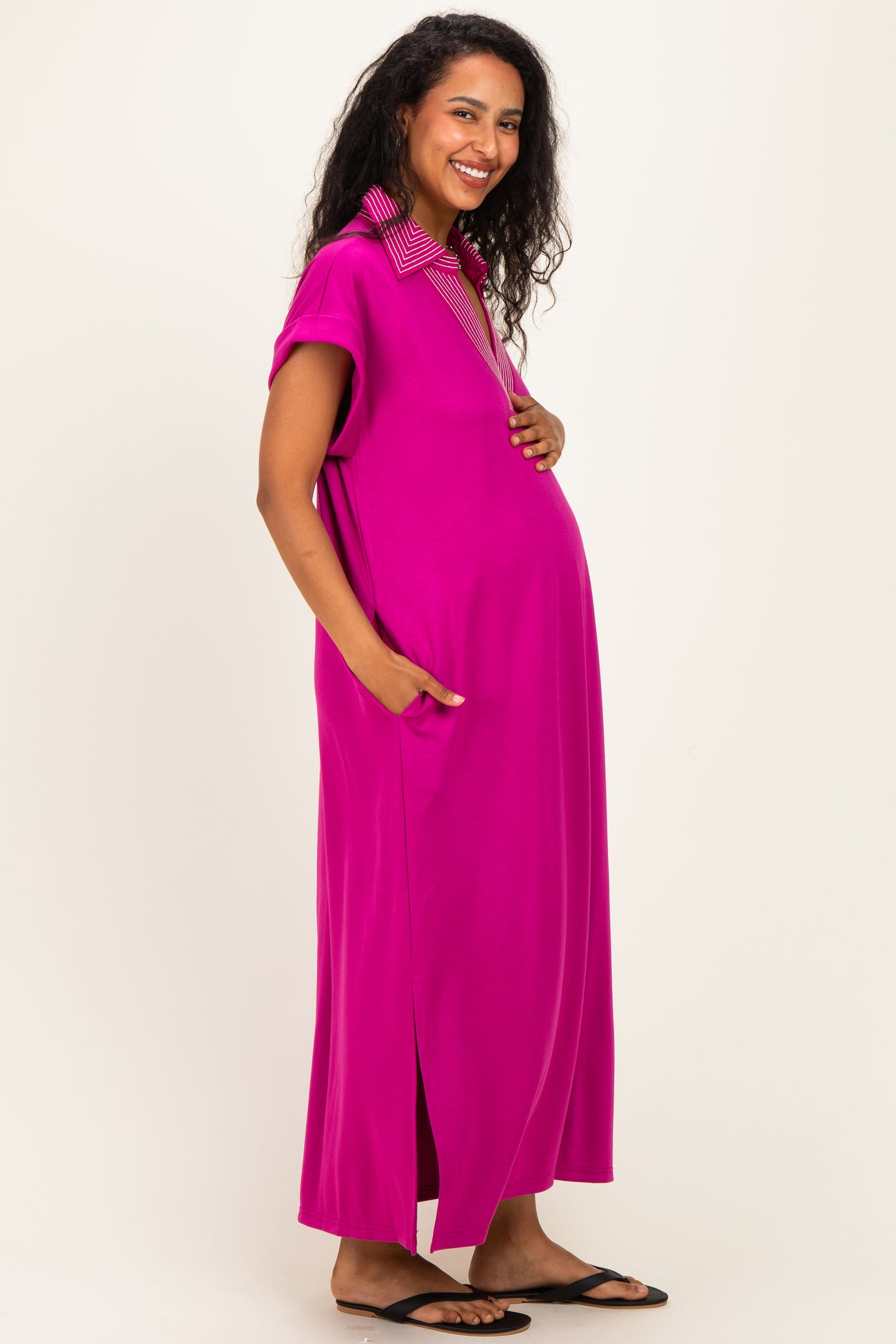 woman wearing a bright pink maternity maxi dress with a checkered collar and pockets, showing her baby bump