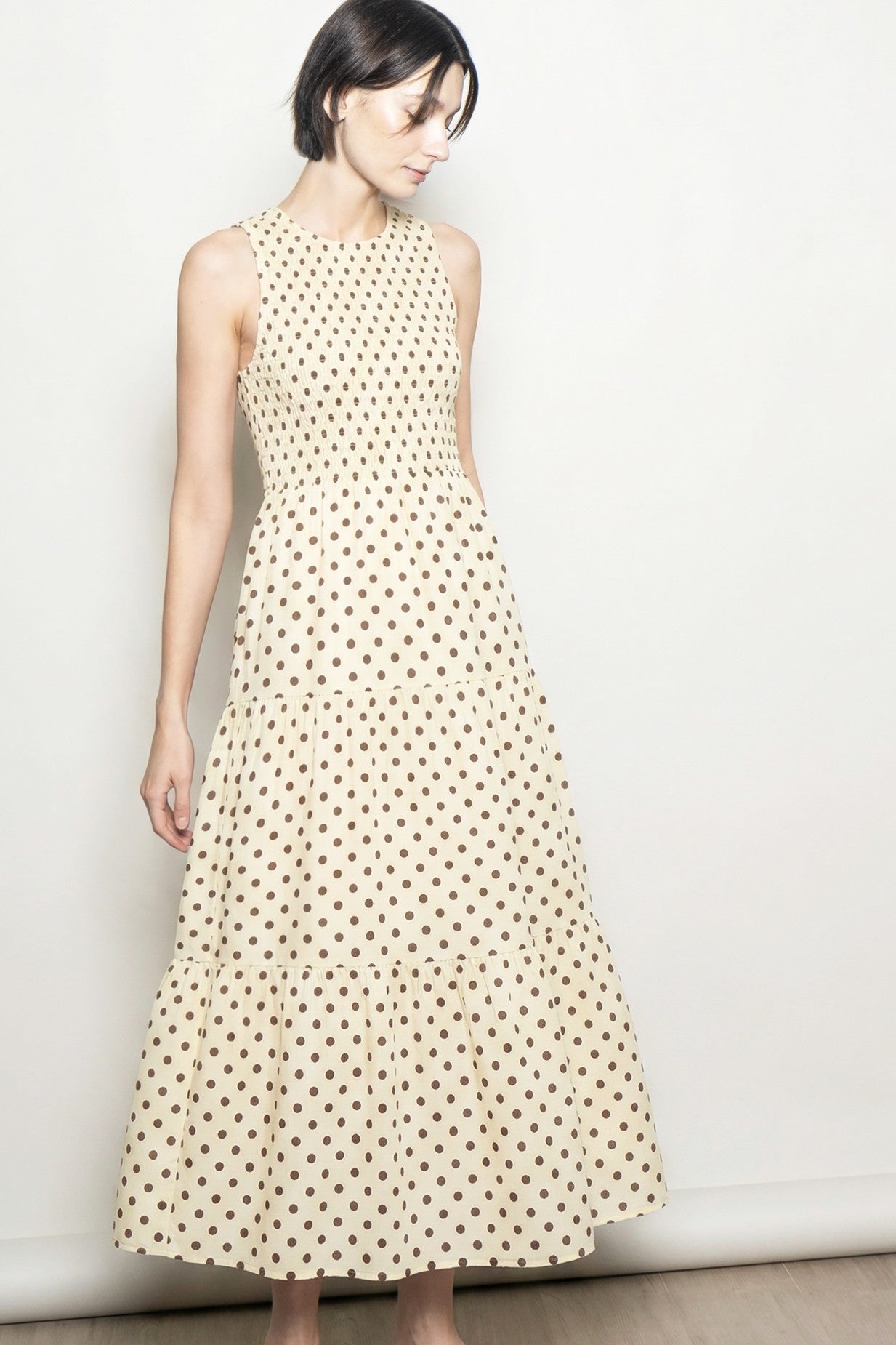 woman wearing a cream tiered maxi dress with brown polka dots and a sleeveless design