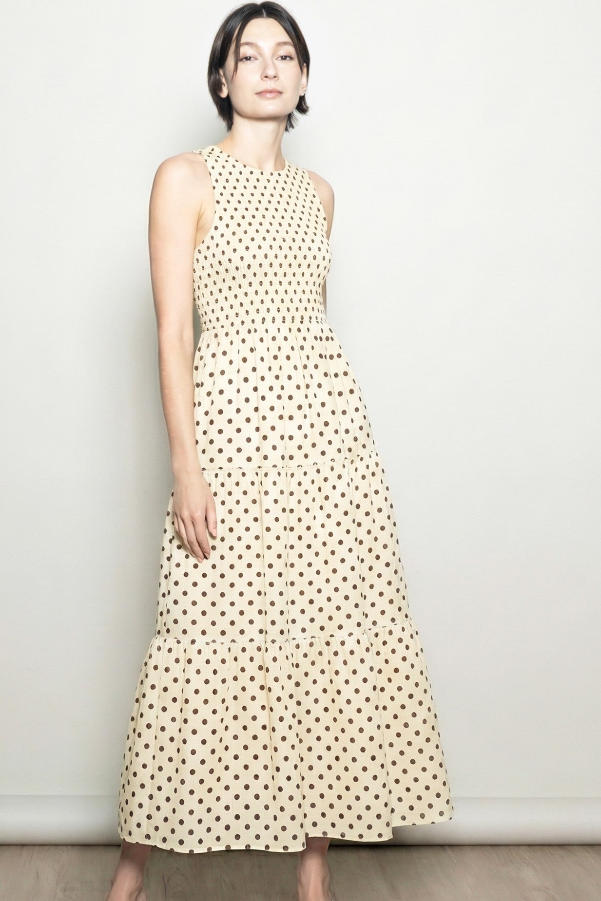 woman wearing a sleeveless cream maxi dress with brown polka dots and a tiered skirt