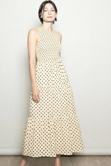 woman wearing a sleeveless cream maxi dress with brown polka dots and a tiered skirt