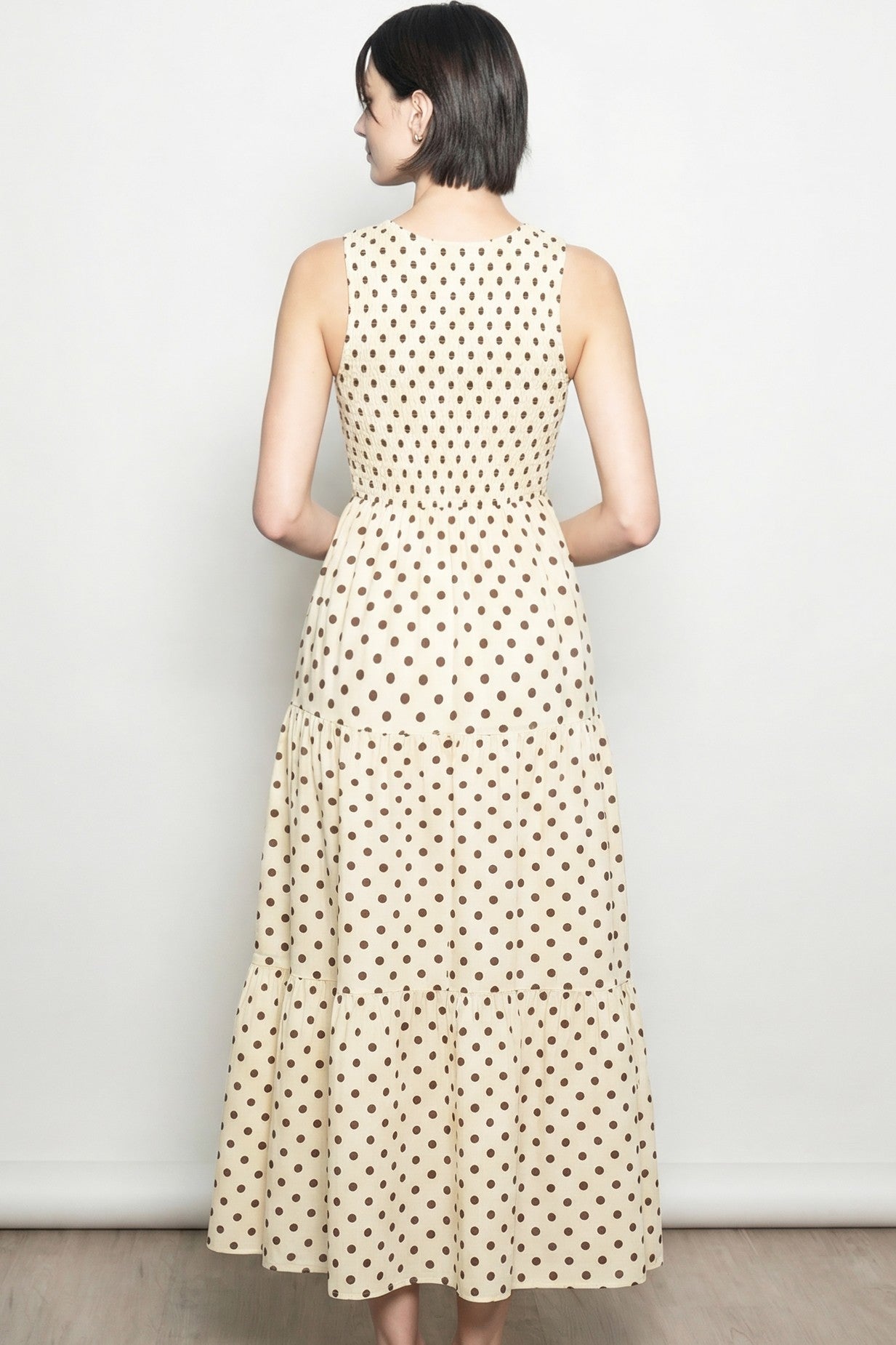 woman wearing a back view of a beige midi dress with a polka dot pattern and a tiered skirt