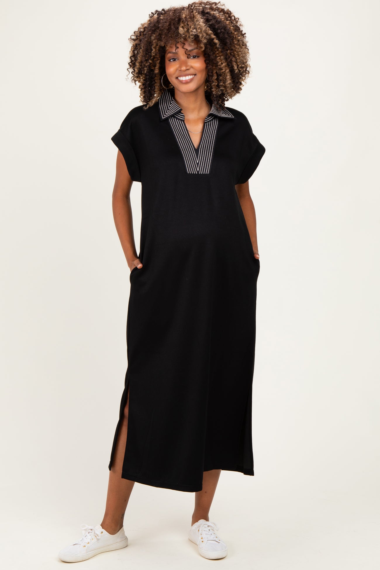woman wearing a black maternity maxi dress with a striped collar and side slits, smiling and showing her baby bump