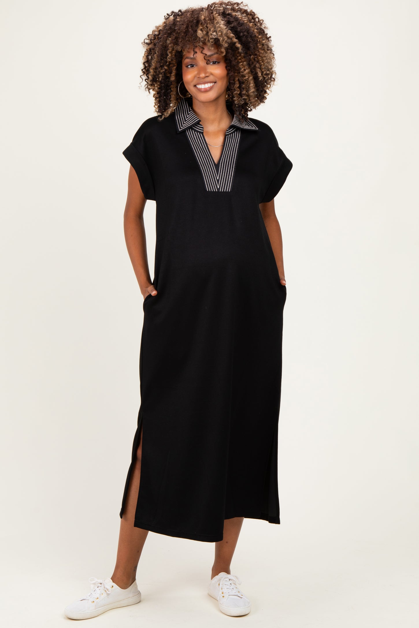 woman wearing a black maternity maxi dress with a striped collar and side slits, smiling and showing her baby bump