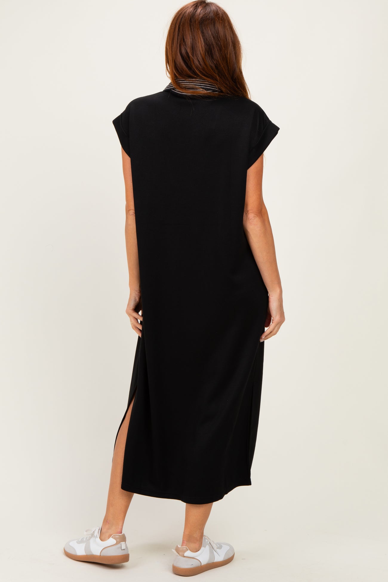 woman wearing a black cap sleeve maxi dress with side slits and styled with white sneakers