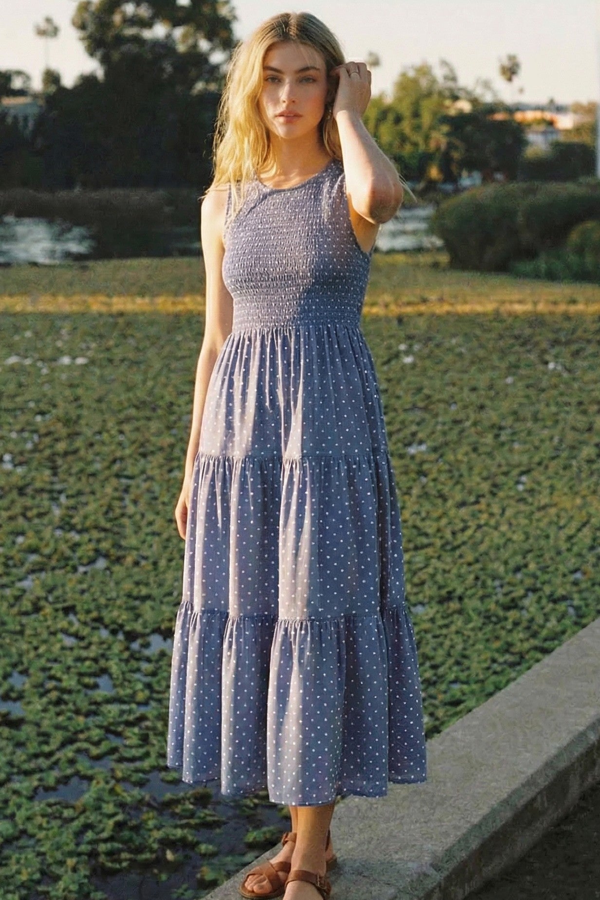 woman wearing a sleeveless blue polka dot maxi dress with a smocked bodice and tiered skirt
