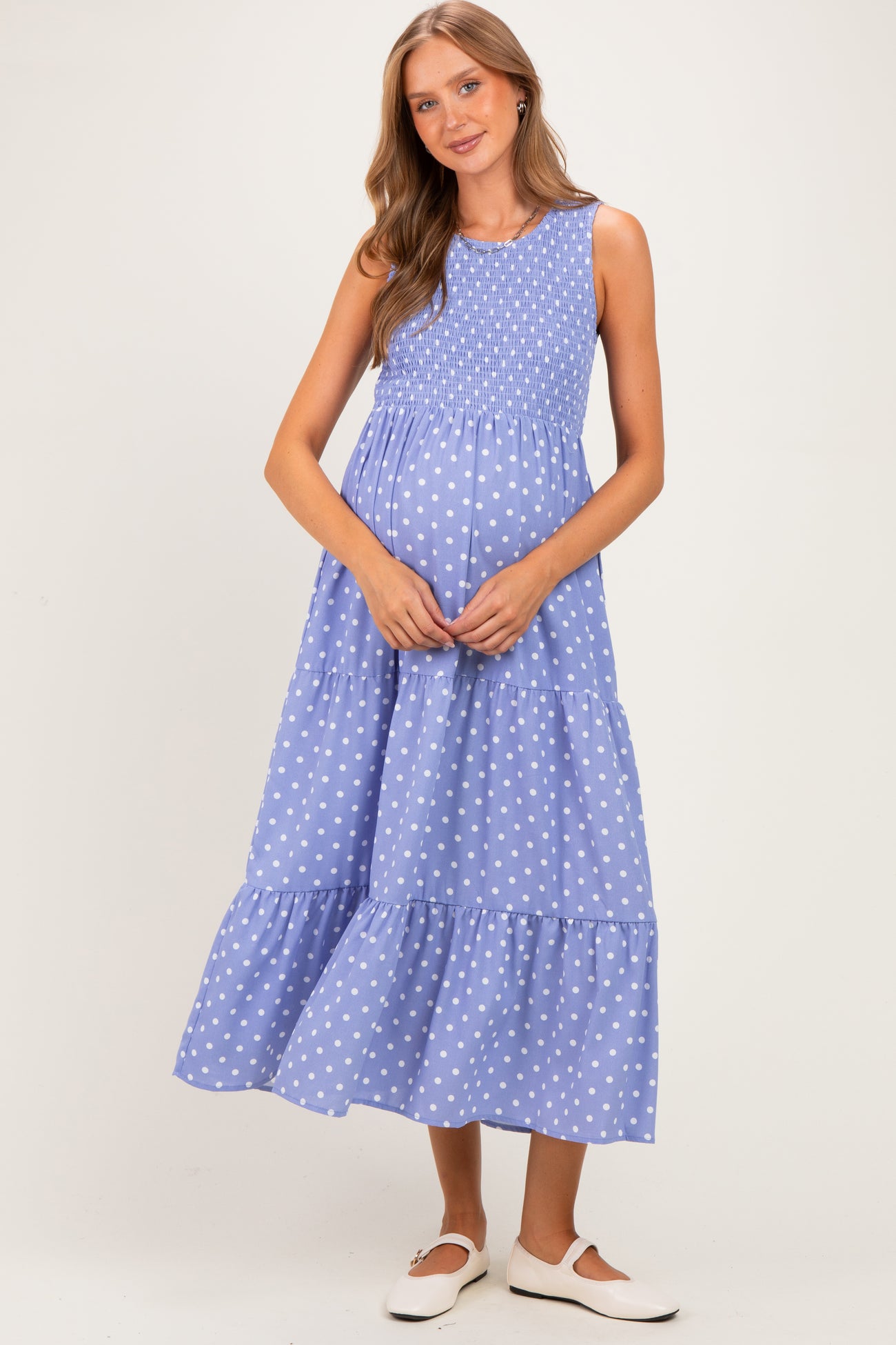 woman wearing a light blue maternity maxi dress with white polka dots and a smocked bodice, holding her baby bump