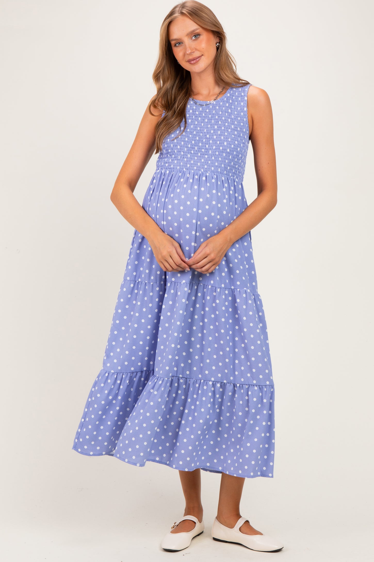 woman wearing a light blue maternity maxi dress with white polka dots and a smocked bodice, holding her baby bump