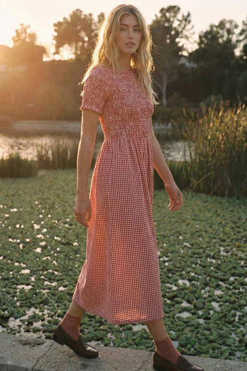 woman wearing a red and white gingham midi dress with short sleeves, standing by a pond during sunset