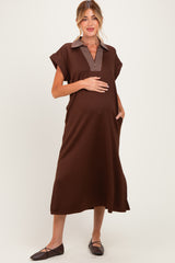 woman wearing a brown maternity dress with a striped collar and pockets, gently cradling her baby bump