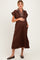 woman wearing a brown maternity dress with a striped collar and pockets, gently cradling her baby bump