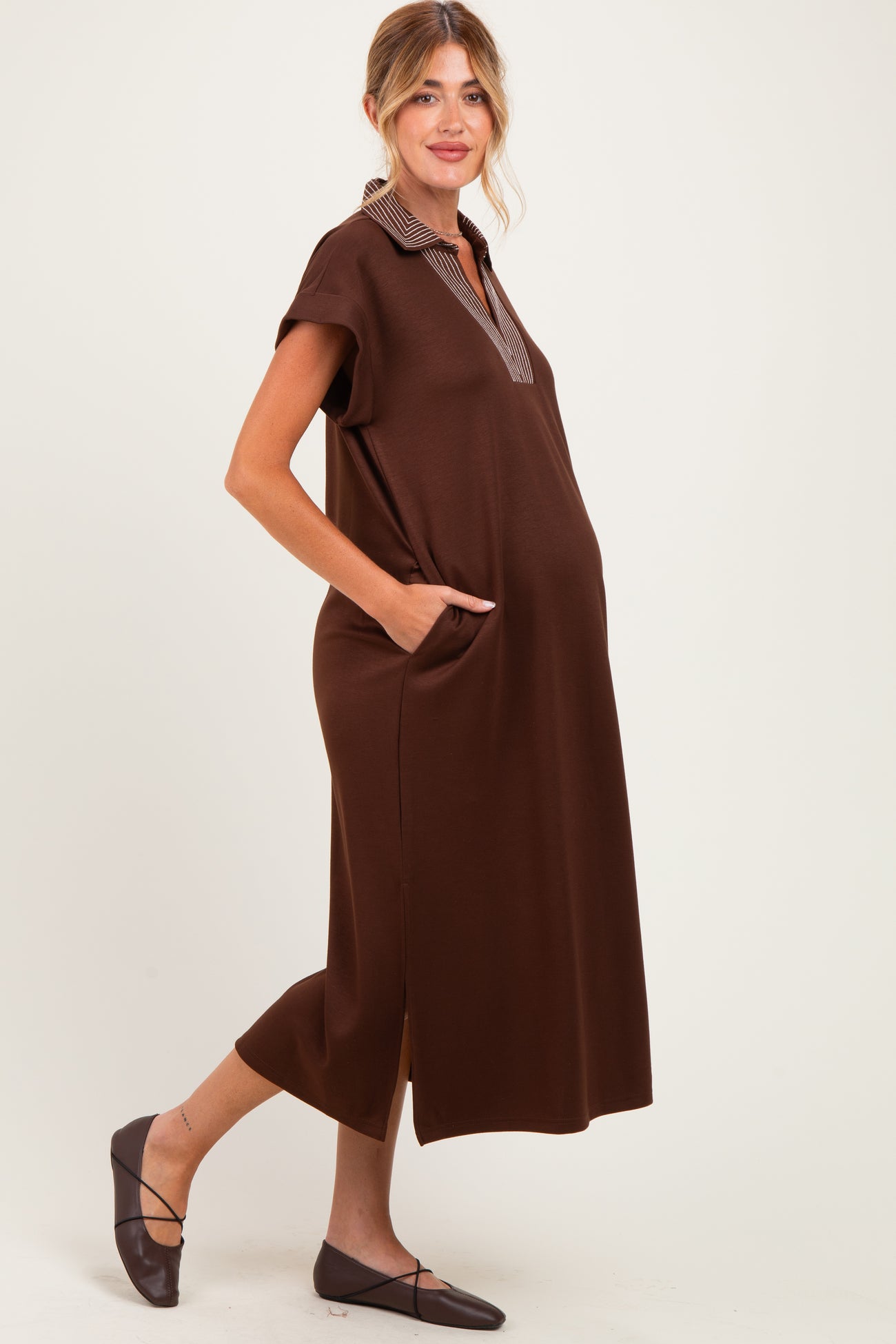 woman wearing a brown maternity dress with short sleeves, a collar, and side pockets, showcasing a visible baby bump