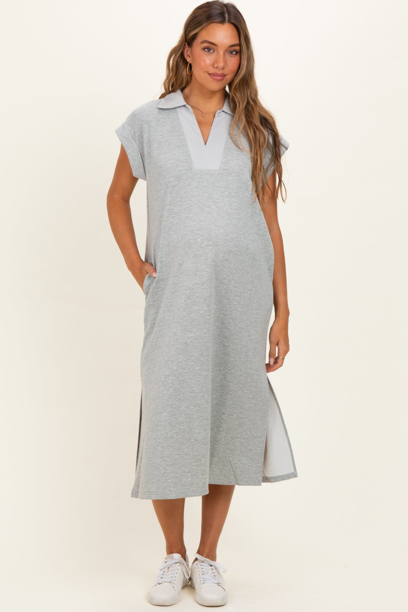 woman wearing a gray maternity dress with a collar, short sleeves, and side slits, standing with hands in pockets