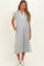 woman wearing a gray maternity dress with a collar, short sleeves, and side slits, standing with hands in pockets