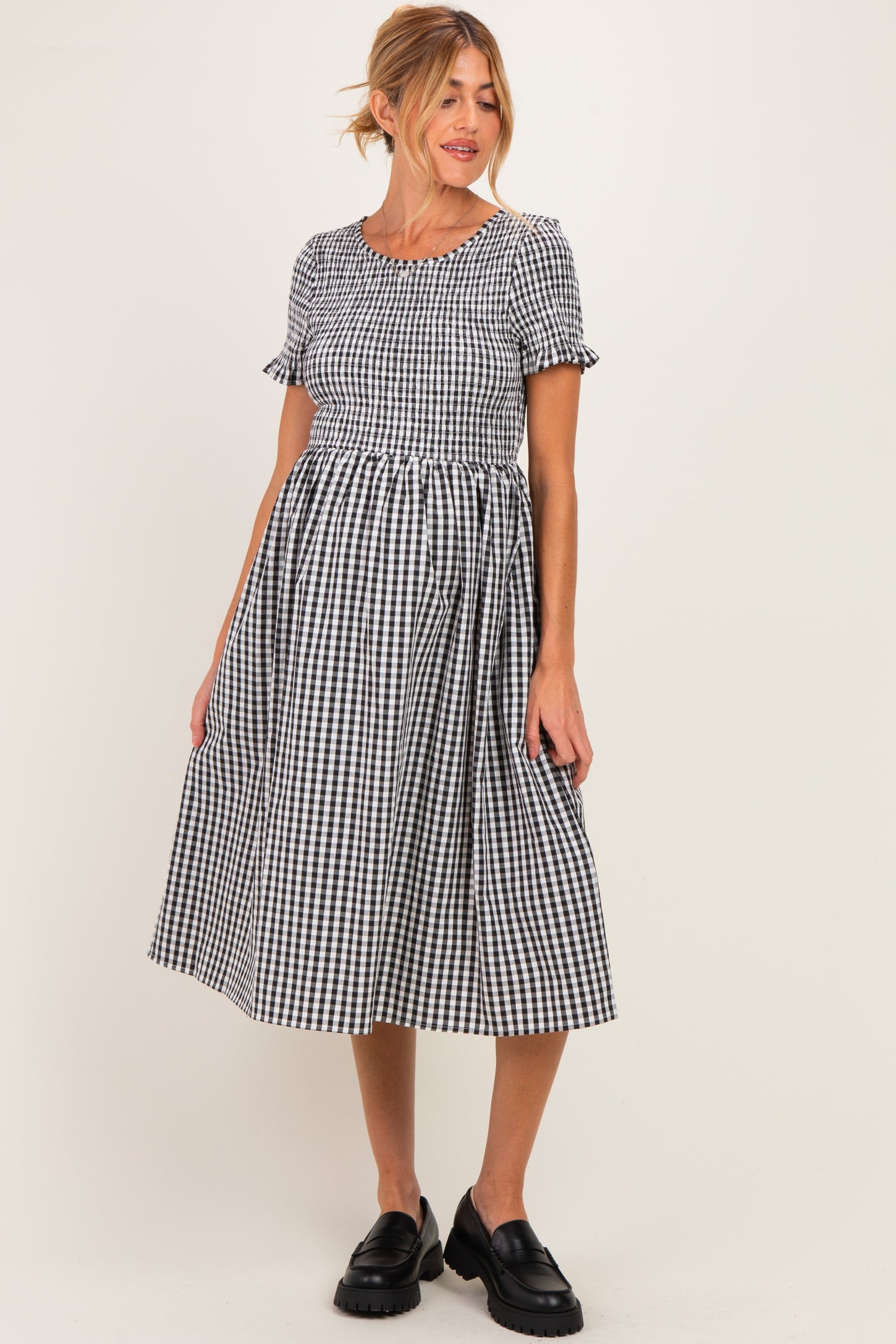 woman wearing a black and white gingham short sleeve maternity dress with a fitted bodice and flowing skirt, showing her baby bump