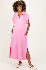 woman wearing a pink maternity maxi dress with a collar and side pockets, featuring a relaxed fit and slits at the sides