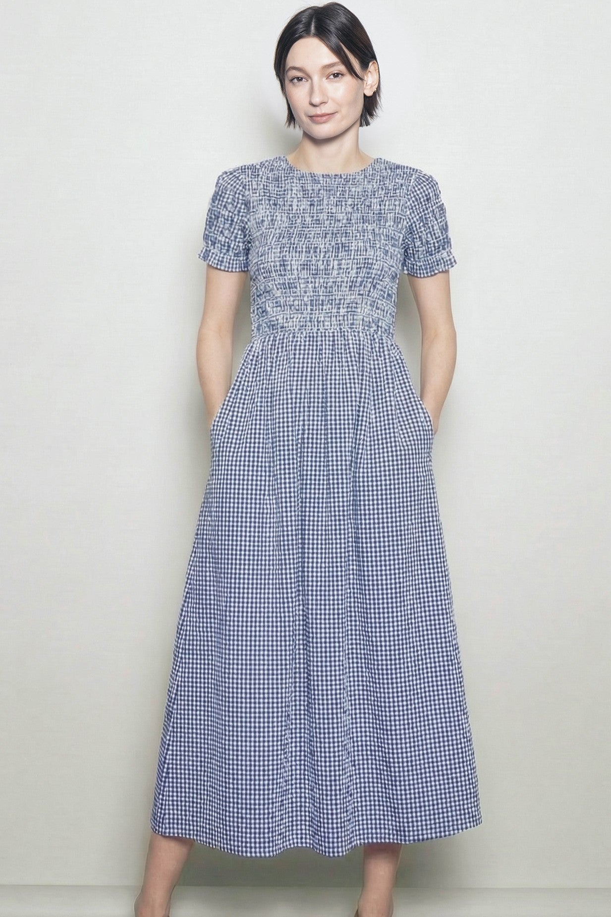 woman wearing a navy and white gingham smocked midi dress with short sleeves and pockets