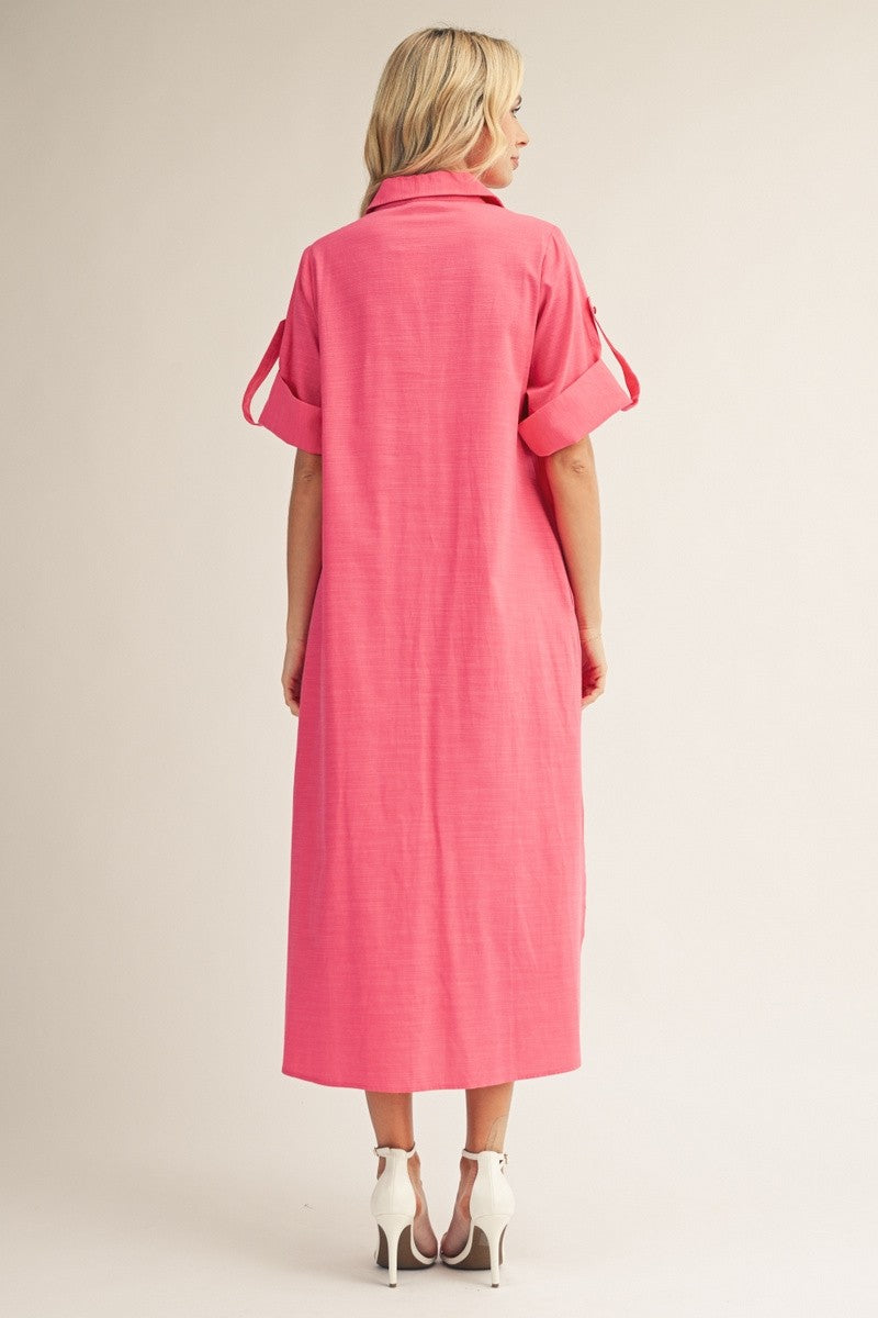 woman wearing a vibrant pink maxi dress with rolled sleeves and a collared neckline, standing with her back to the camera