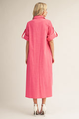 woman wearing a vibrant pink maxi dress with rolled sleeves and a collared neckline, standing with her back to the camera
