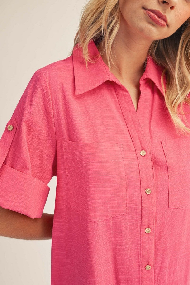 woman wearing a bright pink short sleeve button-up shirt with chest pockets and rolled sleeves