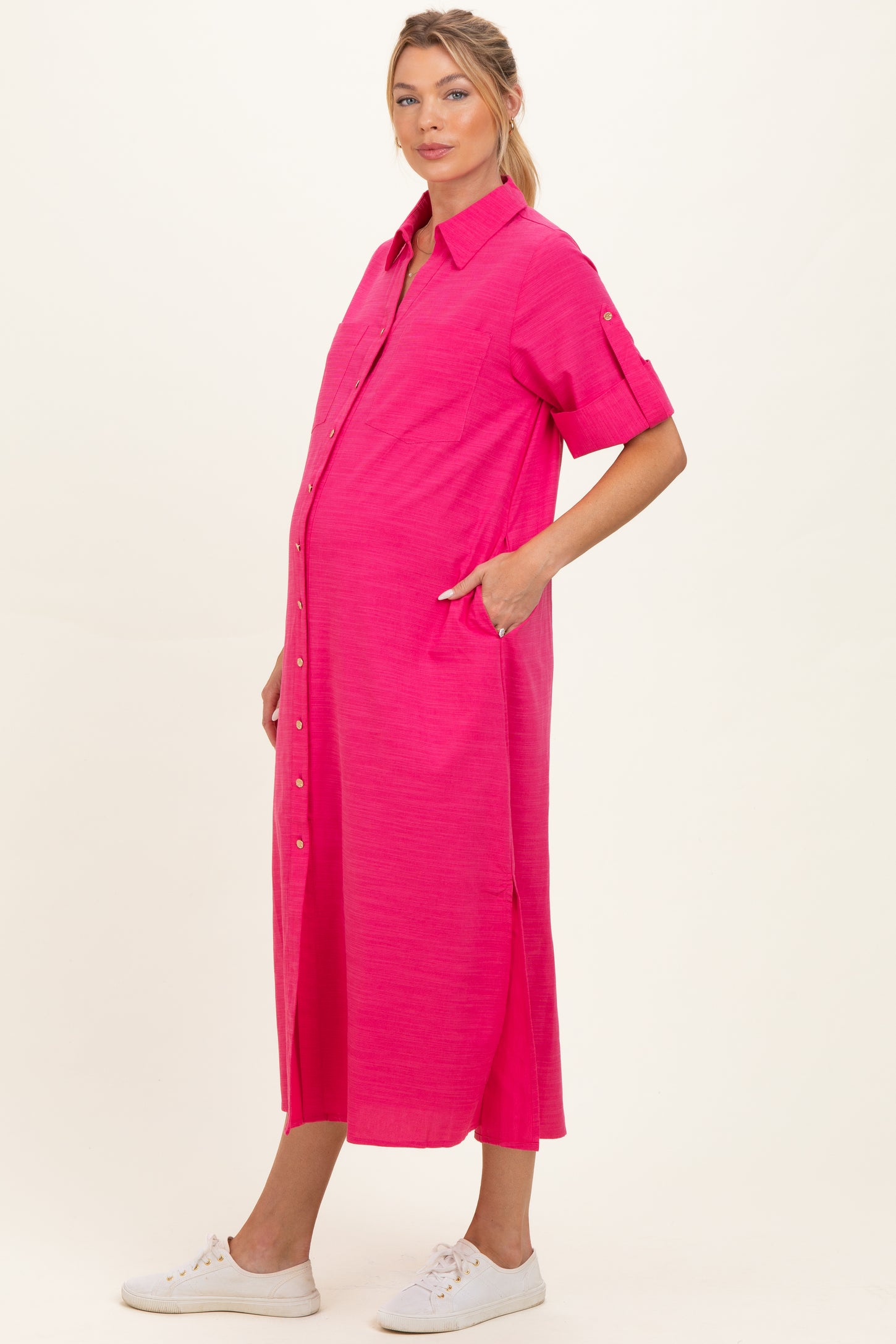 woman wearing a bright pink short sleeve maternity dress with buttons and pockets, showcasing her baby bump
