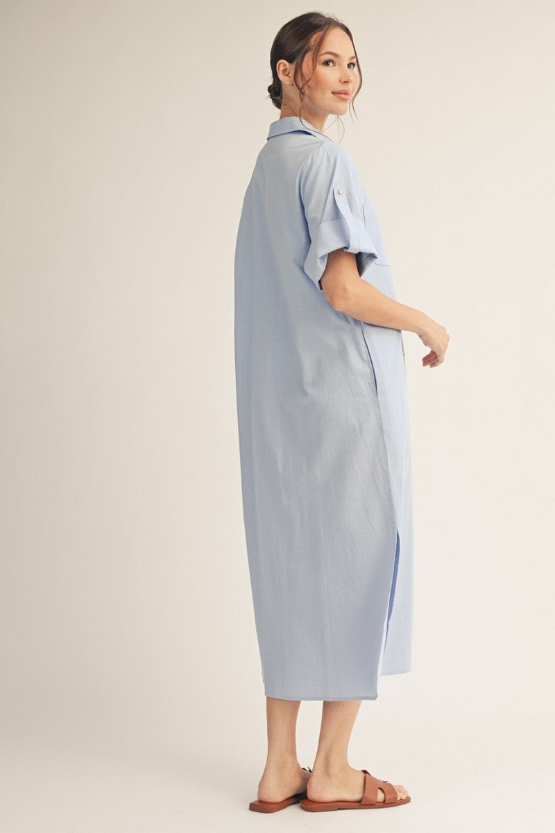 woman wearing a light blue oversized shirt dress with short sleeves and a button detail on the shoulder