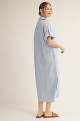 woman wearing a light blue oversized shirt dress with short sleeves and a button detail on the shoulder