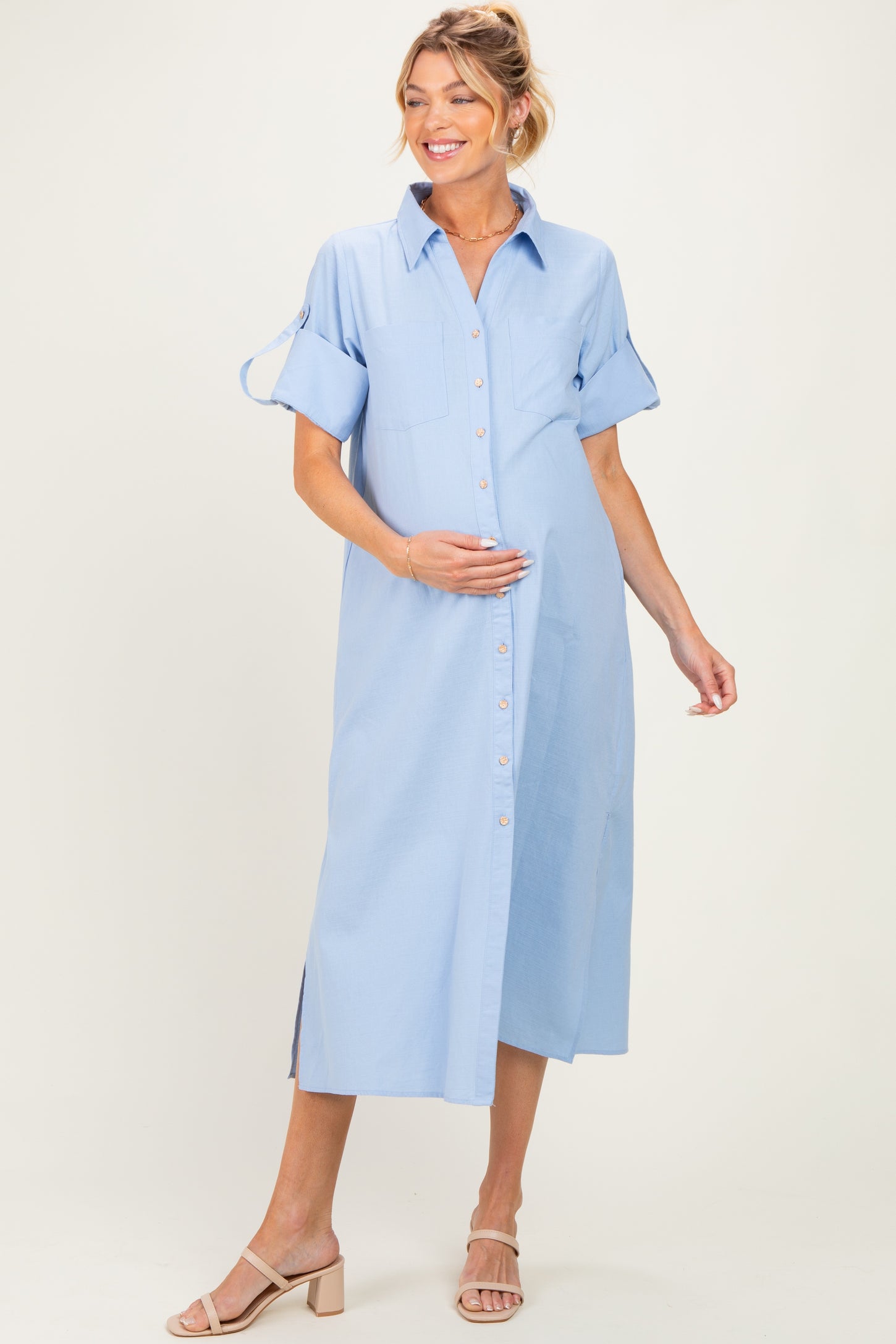 woman wearing a light blue maternity button-up dress with short sleeves and a visible baby bump