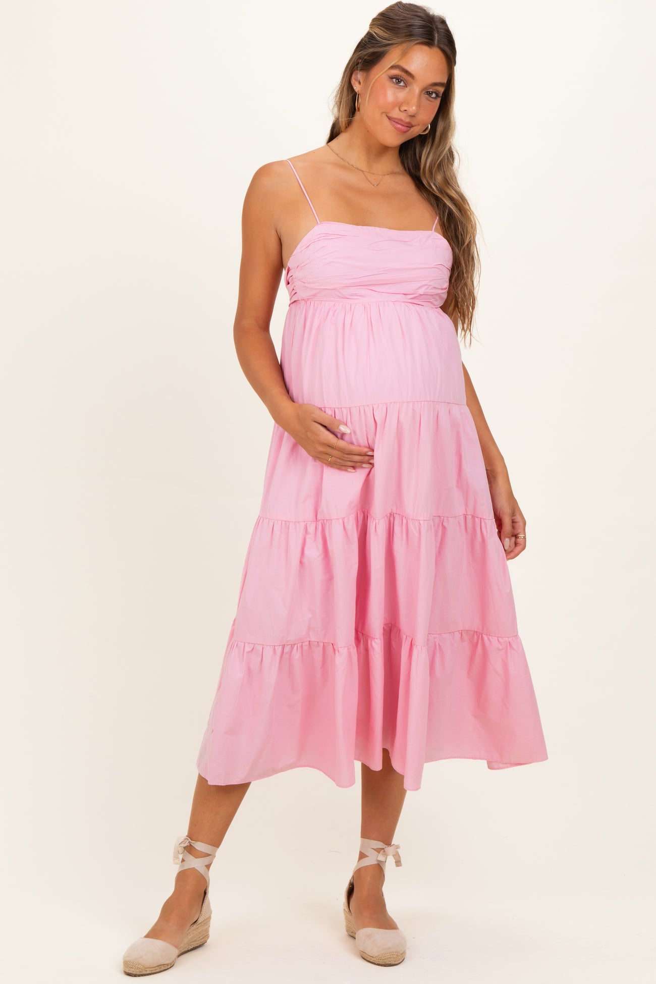 woman wearing a light pink maternity maxi dress with tiered ruffles and a baby bump, posing with one hand on her belly