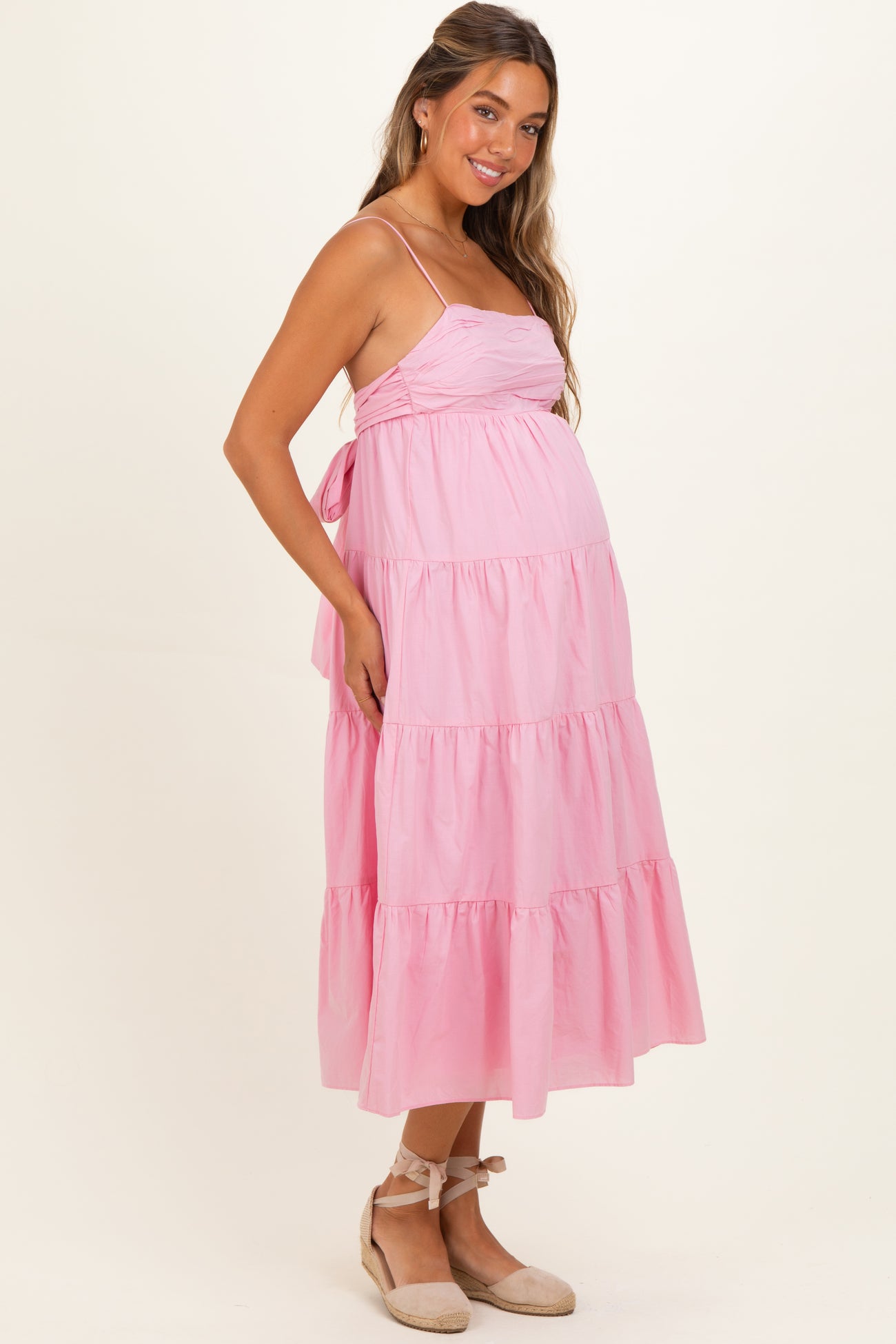 woman wearing a pink tiered maternity dress with spaghetti straps and a visible baby bump