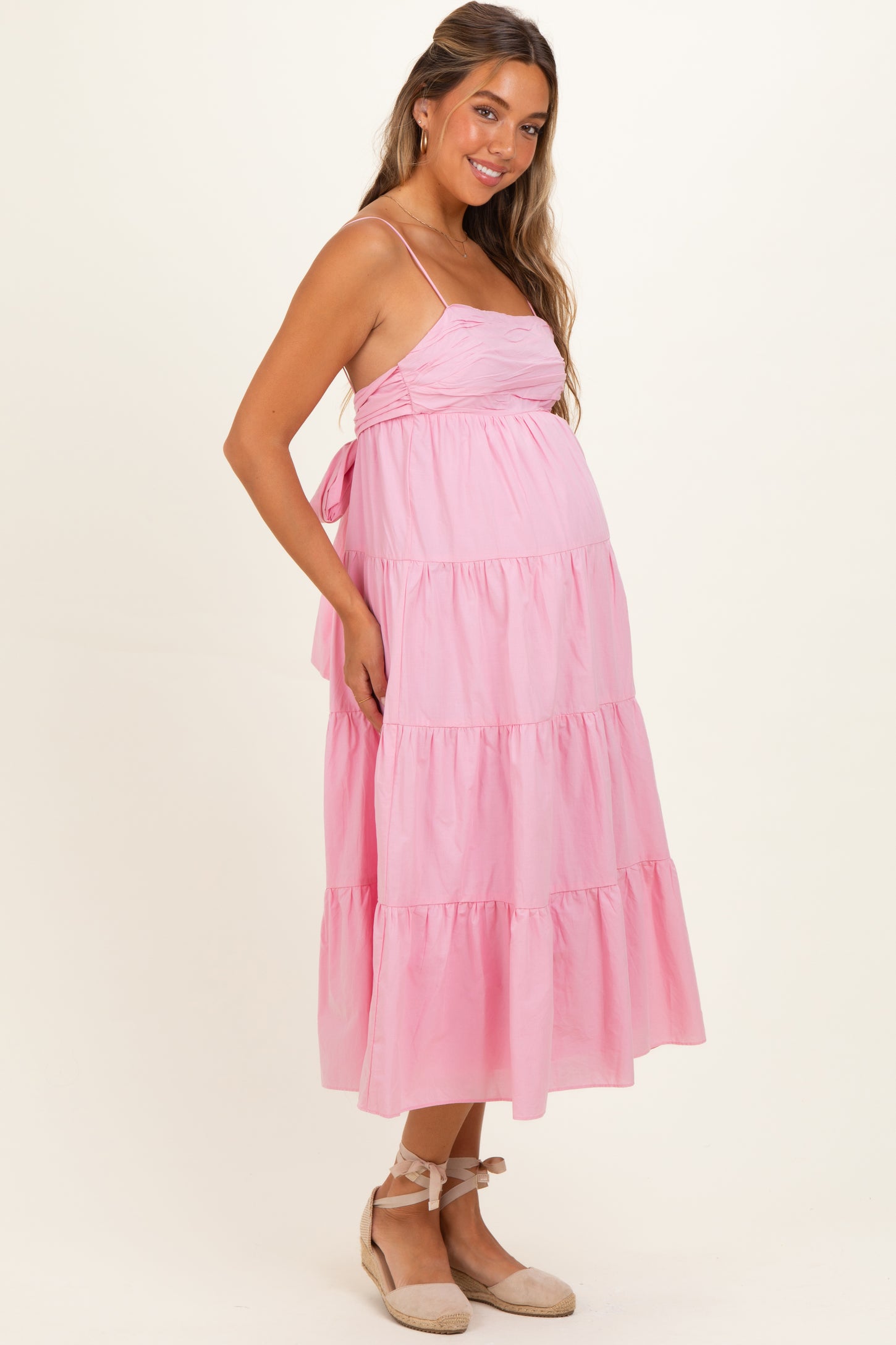 woman wearing a pink tiered maternity dress with spaghetti straps and a visible baby bump