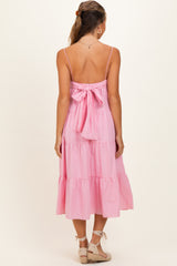 woman wearing a pink maternity dress with a tiered design and a tied back, showing no baby bump