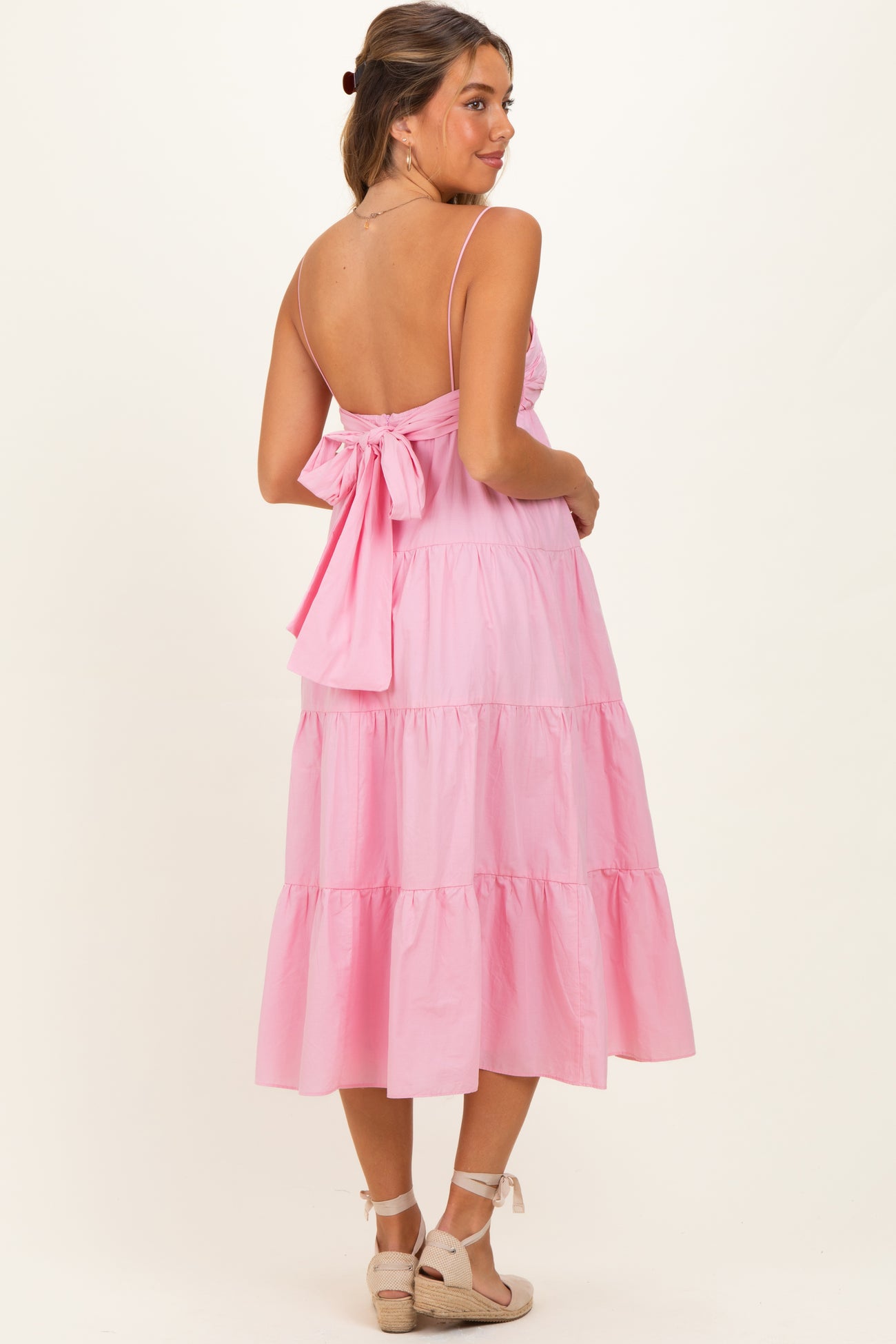 woman wearing a pink tiered maternity dress with a tied back detail and adjustable straps