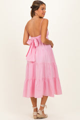 woman wearing a pink tiered maternity dress with a tied back detail and adjustable straps