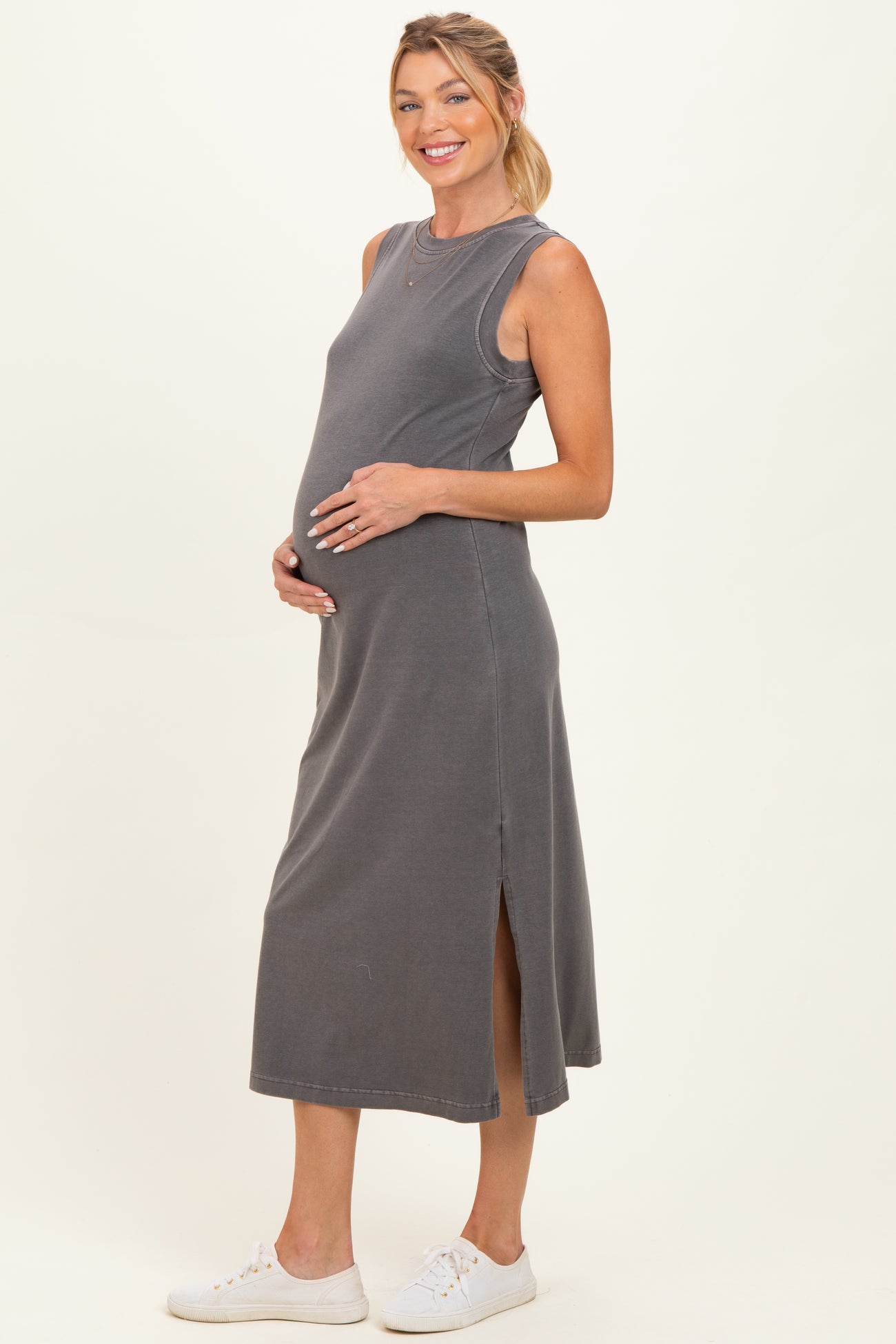woman wearing a grey sleeveless maternity dress with side slits and holding her baby bump
