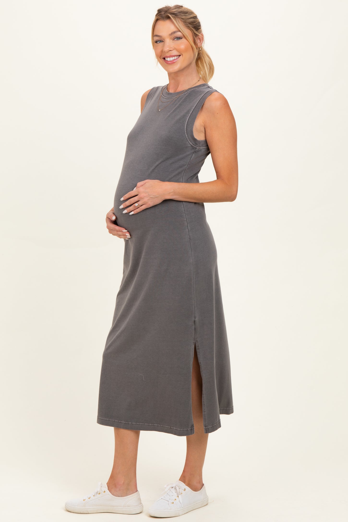 woman wearing a grey sleeveless maternity dress with side slits and holding her baby bump