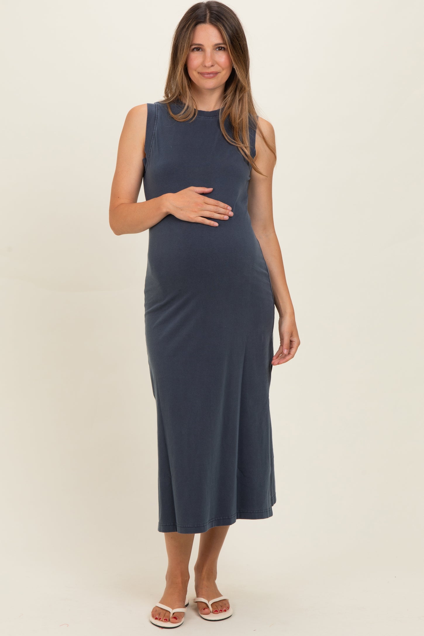 woman wearing a navy blue sleeveless maternity dress with a fitted bodice and open skirt, showcasing her baby bump