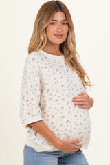 woman wearing a cream floral maternity sweatshirt and holding her baby bump