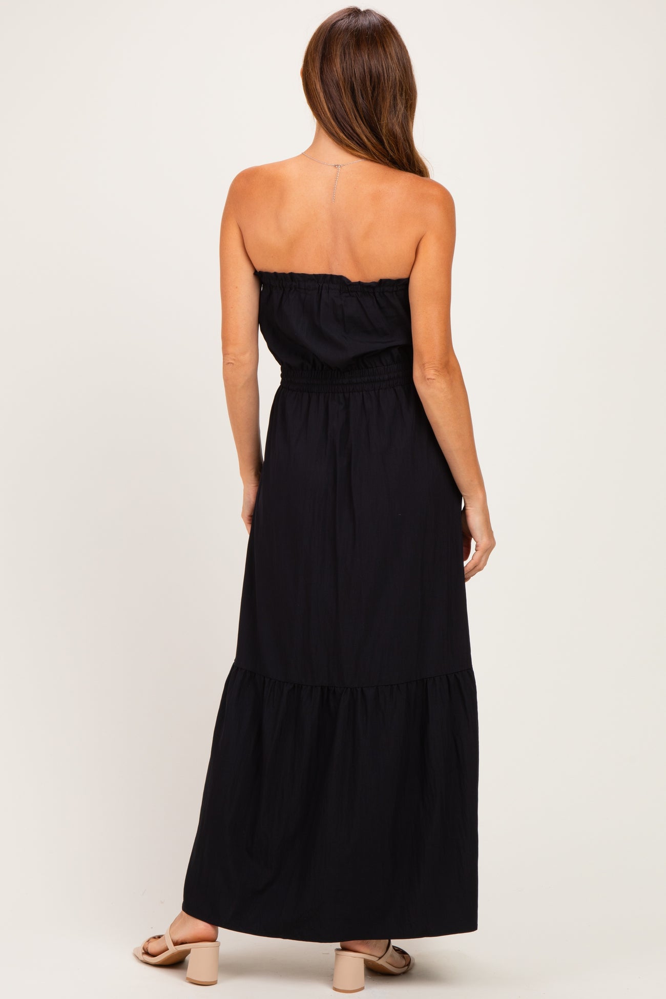 woman wearing a strapless black maxi dress with a smocked bodice and tiered skirt, shown from the back