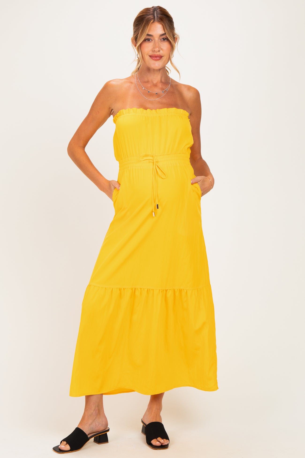 woman wearing a strapless yellow maternity maxi dress with an elastic waist and pockets, standing confidently