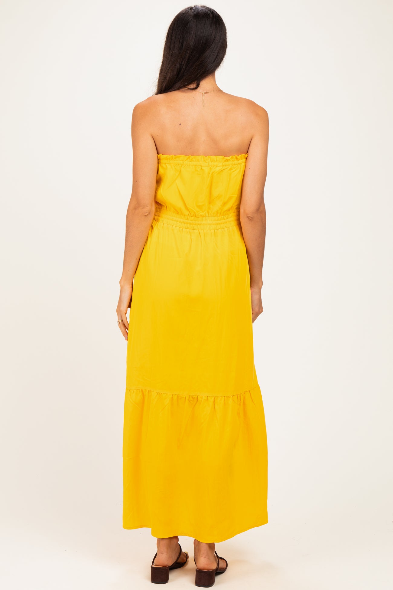 woman wearing a strapless yellow maxi dress with a tiered skirt and an elastic waistband, seen from the back
