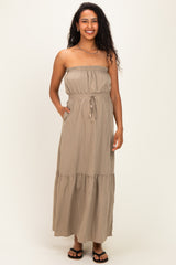 woman wearing a khaki strapless maternity maxi dress with an elastic bodice and tie waist, featuring pockets