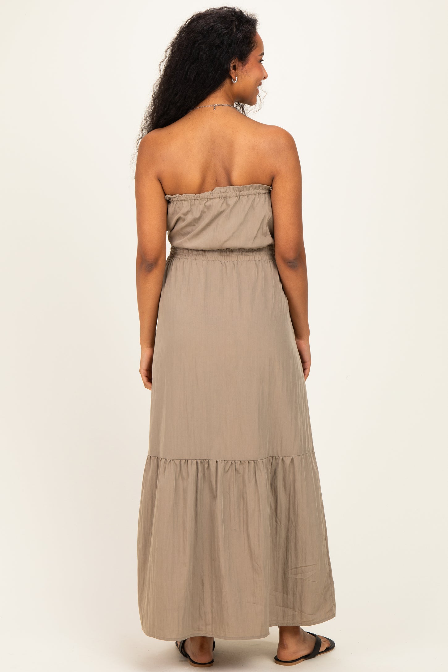 woman wearing a strapless taupe maternity maxi dress with a tiered skirt, showing a baby bump from the back