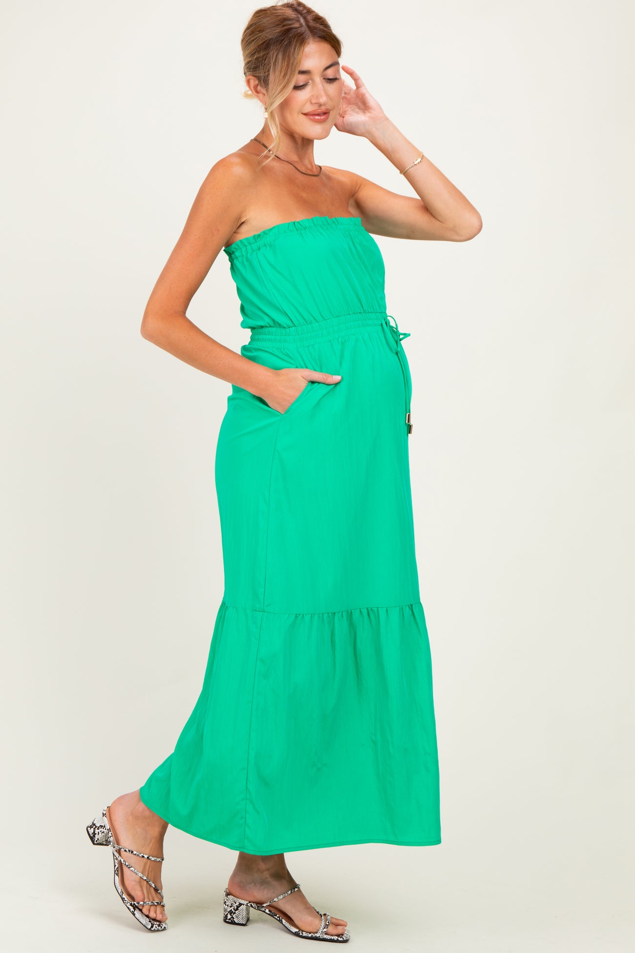 woman wearing a bright green strapless maternity maxi dress with a drawstring waist and pockets, showcasing her baby bump