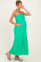 woman wearing a bright green strapless maternity maxi dress with a drawstring waist and pockets, showcasing her baby bump