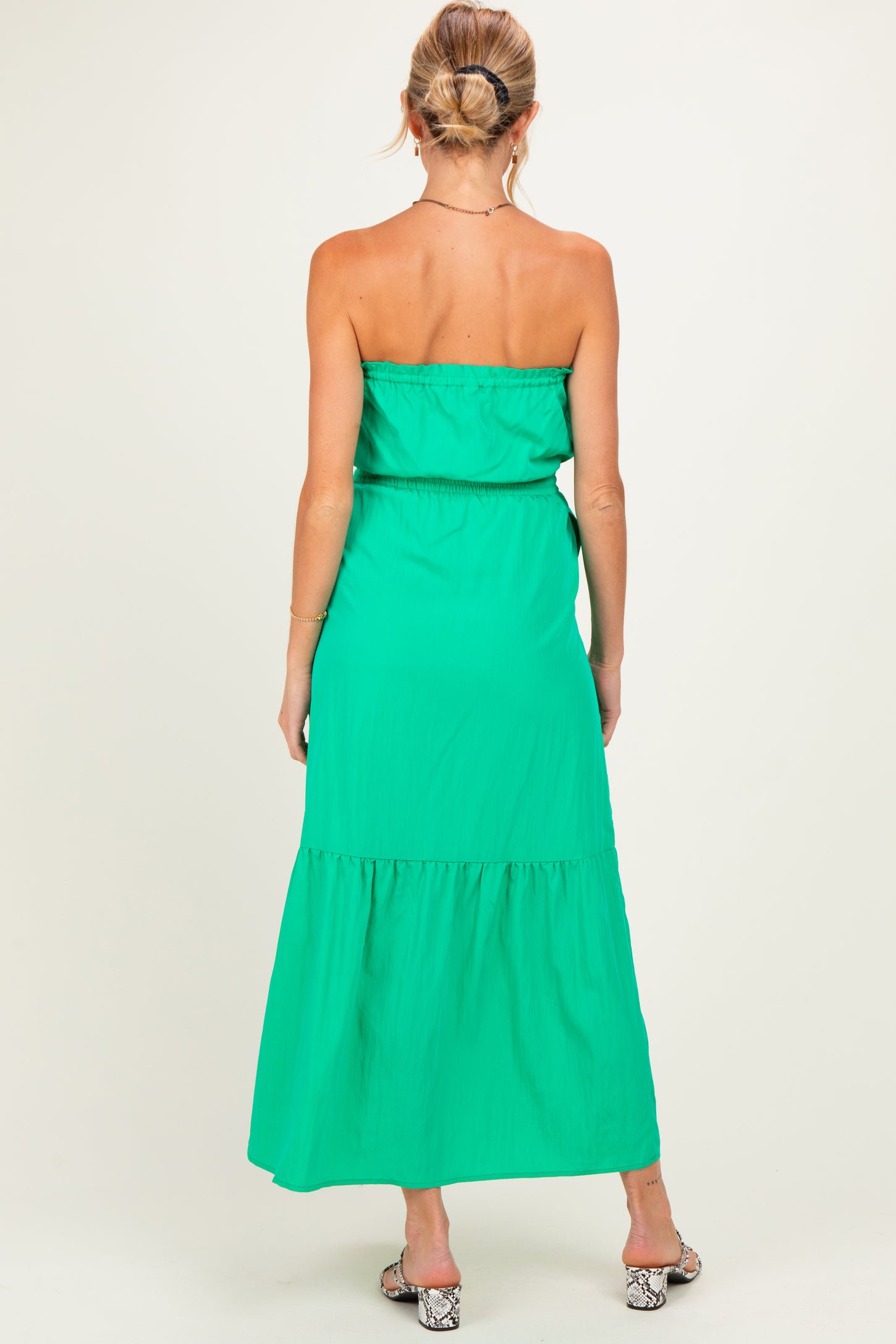 woman wearing a strapless green maternity maxi dress with a tiered hem and an elastic waistband