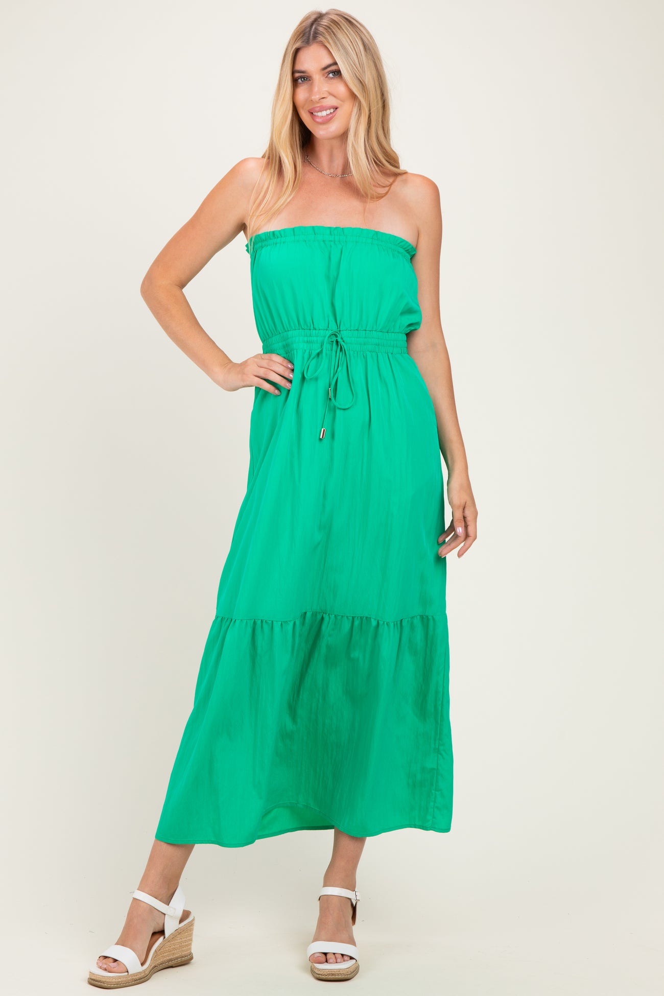 woman wearing a green strapless maxi dress with an elastic waistband and tiered skirt, standing in a neutral background