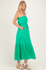 woman wearing a green strapless maxi dress with pockets and a tiered hem, paired with wedge sandals