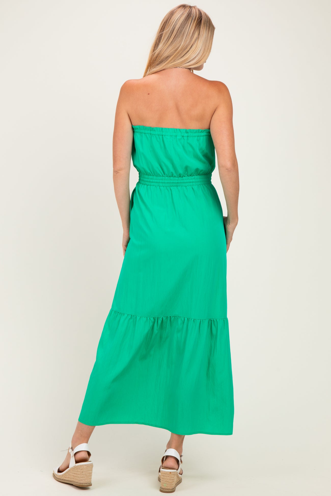 woman wearing a green strapless maxi dress with a tiered skirt and an elastic waistband, viewed from the back