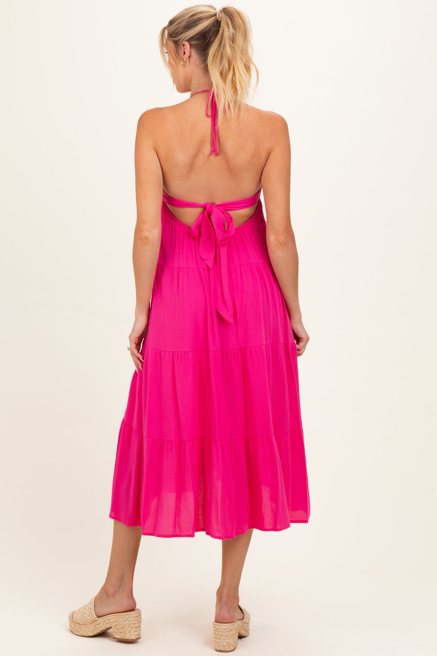woman wearing a bright pink maternity dress with a halter neck and open back design, showing a baby bump