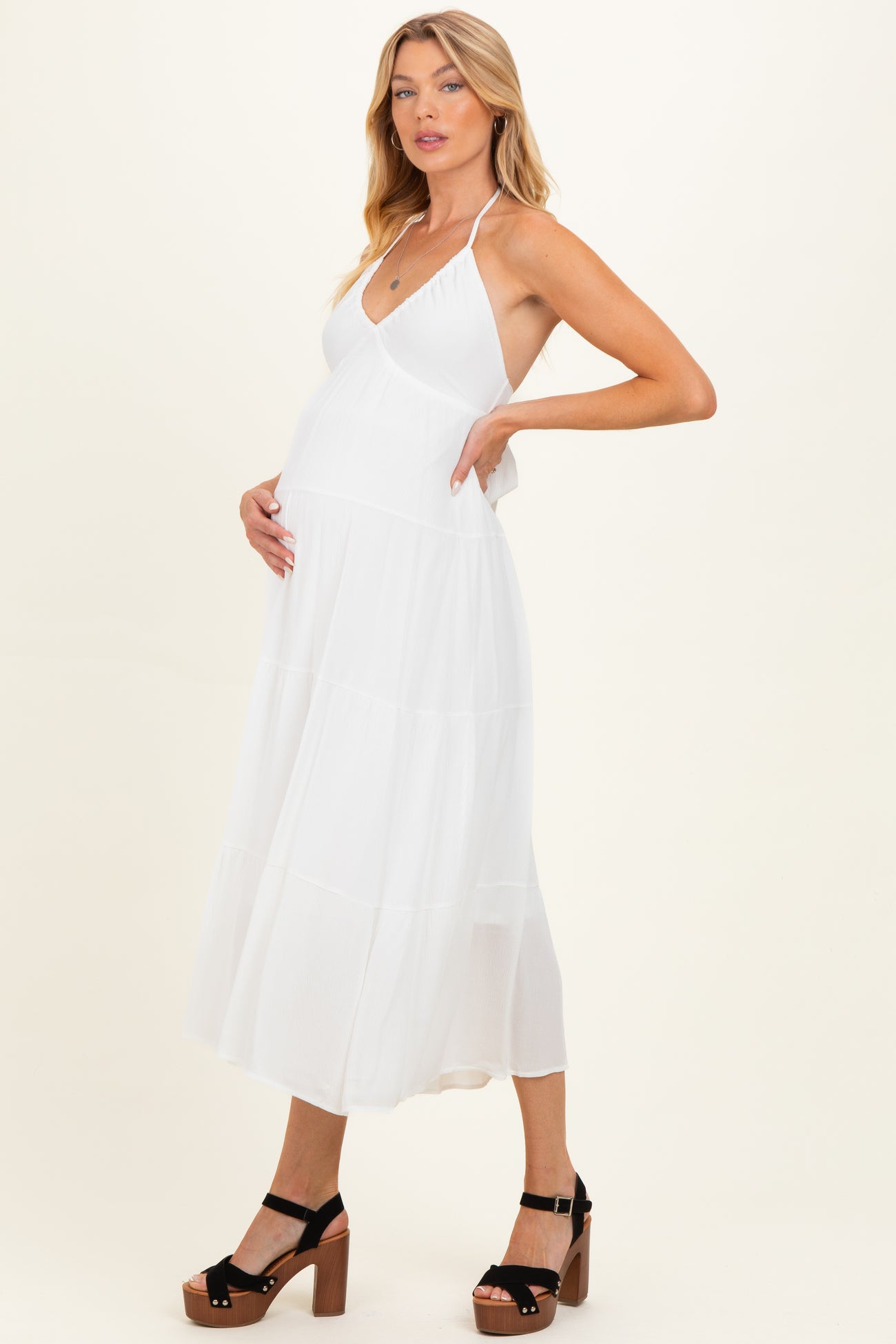woman wearing a white halter neck maternity dress and cradling her baby bump